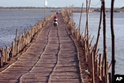 Cambodians ride across a Mekong bamboo bridge in Kom pong Cham, Cambodia Saturday, Dec. 20, 2014. The bridge is constructed every dry season for locals to travel over. The bridge is taken down before the wet session comes to prevent it being washed away.
