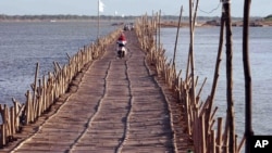 Cambodians ride across a Mekong bamboo bridge in Kom pong Cham, Cambodia Saturday, Dec. 20, 2014. The bridge is constructed every dry season for locals to travel over. The bridge is taken down before the wet session comes to prevent it being washed away. (AP Photo/Nick Ut)