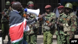 A supporter of presidential candidate Raila Odinga demonstrates as Kenyan policemen keep vigil outside the Supreme Court in Nairobi, Mar. 30, 2013.