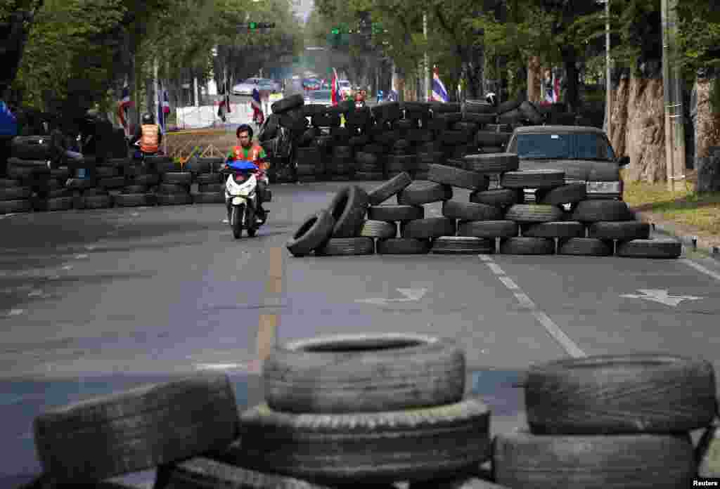 A motorcyclist rides past barricades constructed by anti-government protesters during a rally outside the Government House in Bangkok, Thailand, Dec. 29, 2013. 