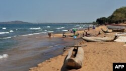 FILE - People wash clothes on Saga Beach as traditional boats are left by the seaside, at Lake Malawi, July 17, 2011. 