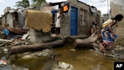 A woman carrying a baby on her back jumps as she tries to avoid stepping on the dirty water in Beira, Mozambique, Wednesday, March 27, 2019. (AP Photo/Themba Hadebe)