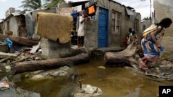 A woman carrying a baby on her back jumps as she tries to avoid stepping on the dirty water in Beira, Mozambique, Wednesday, March 27, 2019. (AP Photo/Themba Hadebe)