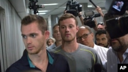 Journalists surround American Olympic swimmers Gunnar Bentz, left, and Jack Conger, center, as they leave the police station at Rio International airport early Aug. 18, 2016. 