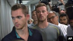 Los periodistas acompañan a Gunnar Bentz, izquierda, y Jack Conger, centro, a la salida de la estación de la policía del aeropuerto internacional de Rio.