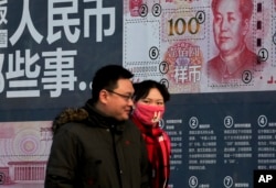 A couple walk past a display showing the security features of the new 100 Yuan note in Beijing, Monday, Jan. 11, 2016.