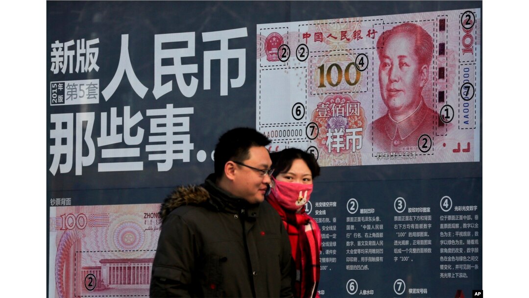 A couple walk past a display showing the security features of the new 100 Yuan note in Beijing, Jan. 11, 2016.