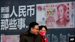 A couple walk past a display showing the security features of the new 100 Yuan note in Beijing, Monday, Jan. 11, 2016.