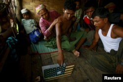 FILE - Abdhulami, center, 22, who was released from a human trafficking boat, points at pictures of people he recognises from the boat as he rests at a refugee camp outside Sittwe, Myanmar May 27, 2015. When the Myanmar navy seized the boat used by people smugglers.