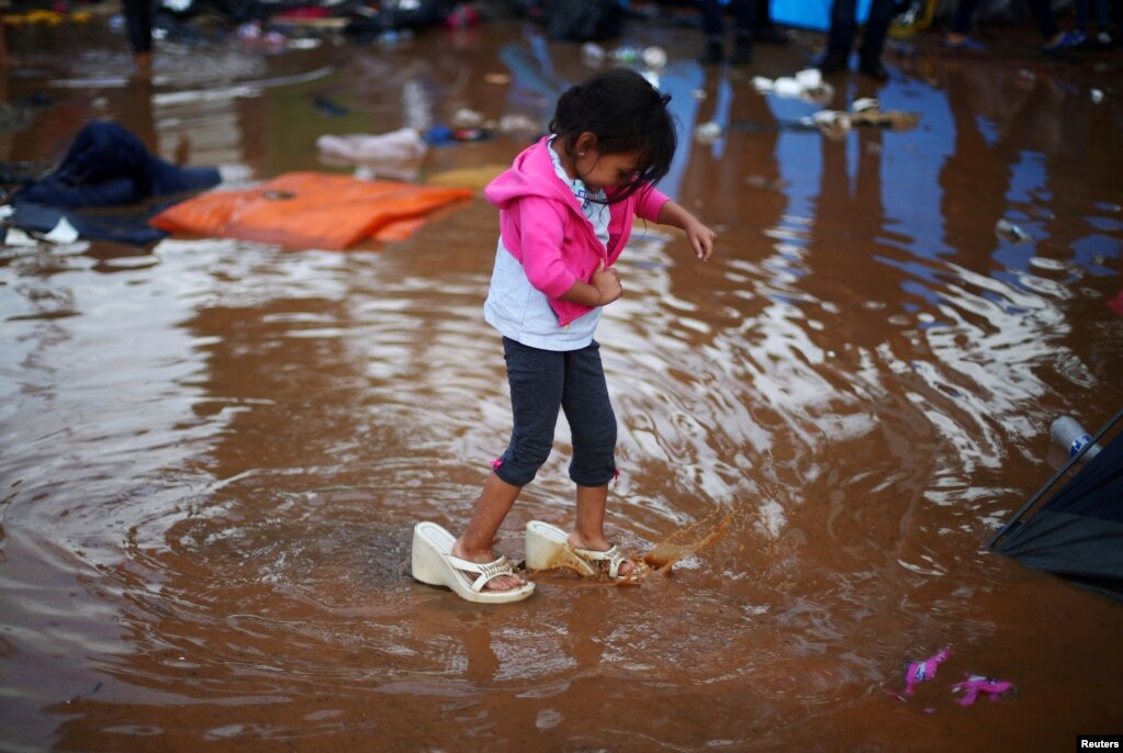 폭우가 내린 멕시코 티후아나의 캐러밴 임시 캠프에서 소녀가 엄마 구두를 신은 채 침수된 도로를 건너고 있다.&nbsp;