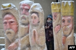 A girl smokes as she found a shelter from a snow fall behind sculptures depicting the nativity scene, in the center of western Ukrainian city of Lviv, Dec. 20, 2017.