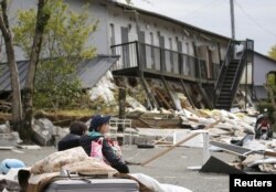 A university student takes a rest in front of an apartment building ravaged by earthquakes in Minamiaso town, Kumamoto prefecture, southern Japan, in this photo taken by Kyodo, April 16, 2016.