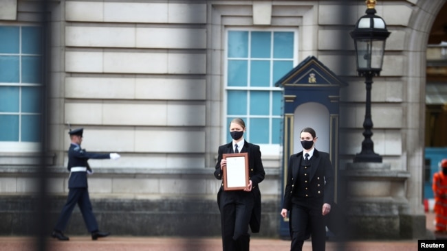بکنگھم پیلس کے عملے کے ارکان شہزادہ فلپ کے انتقال کا سرکاری اعلان محل کے دروازے پر چسپاں کرنے کے لیے آ رہے ہیں۔