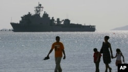 FILE - A Filipino family stroll the beach at Subic Bay as the USS Harpers Ferry approaches to dock, Feb. 17, 2006. 