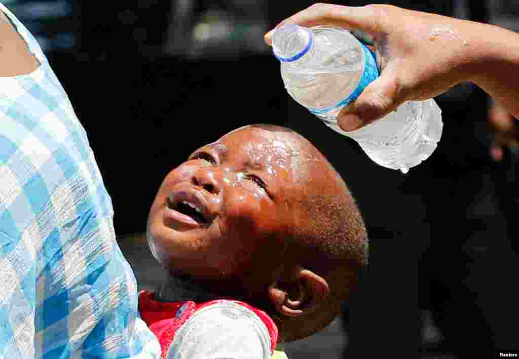 A woman pours water over a child affected by teargas after clashes between police and street vendors in central Harare, Zimbabwe.