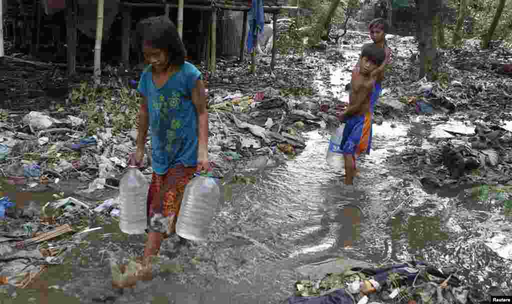 Children carry plastic containers of potable water as they wade through debris and mud brought by Typhoon Rammasun in Batangas city, south of Manila, July 17, 2014.