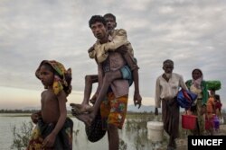 FILE - Rohingya refugees who crossed the Naf River, which demarcates the border between Myanmar and Bangladesh, on makeshift rafts made of logs, bamboo poles and jerrycans, walk along an embankment.