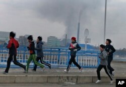 FILE - Young joggers pass by as smoke billows from the stack of the Pyongyang Power Plant in Pyongyang, North Korea, Dec. 15, 2018.