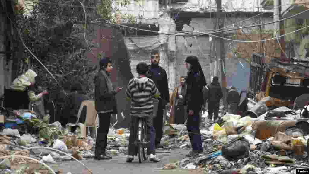 Civilians stand along a street amid garbage and rubble of damaged buildings in the besieged area of Homs, Jan. 27, 2014.