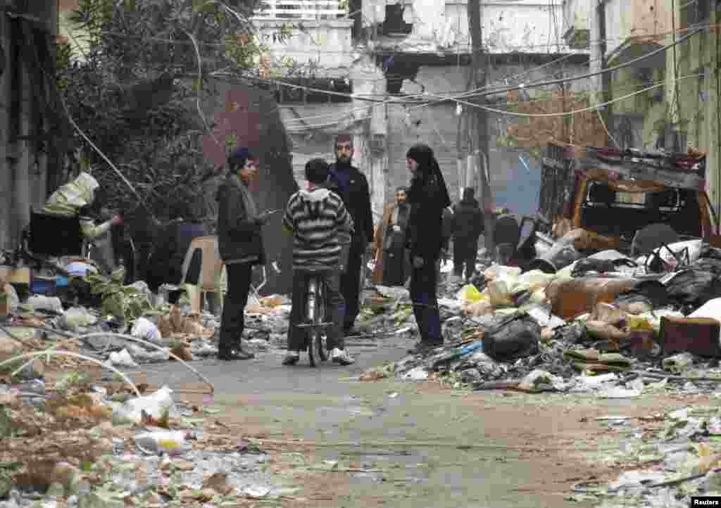 Civilians stand along a street amid garbage and rubble of damaged buildings in the besieged area of Homs, Jan. 27, 2014. 