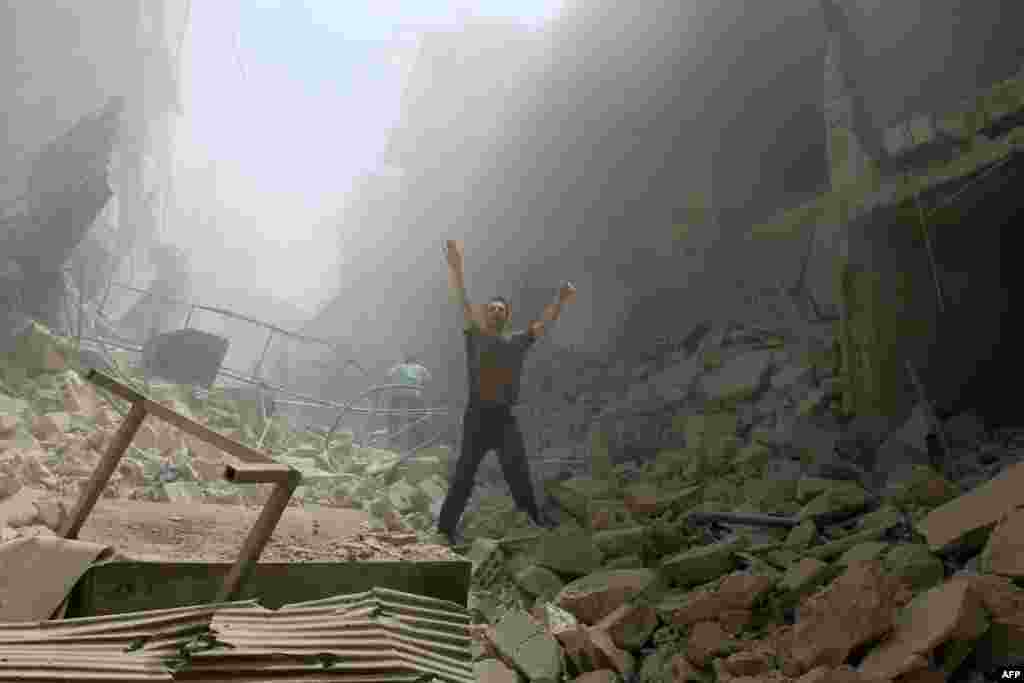 Seorang pria mengacungkan tangannya di tengah puing-puing bangunan menyusul serangan udara di daerah al-Kalasa di Aleppo, Suriah (28/4). (AFP/Ameer Alhalbi)
