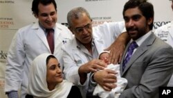 Fatema Al Ansari dari Qatar (kiri), melihat dokternya Salih Yasin merapikan kain pembungkus bayi yang digendong suaminya, Khalifa Alhayal di Rumah Sakit Jackson Memorial, Miami. (AP/Lynne Sladky)