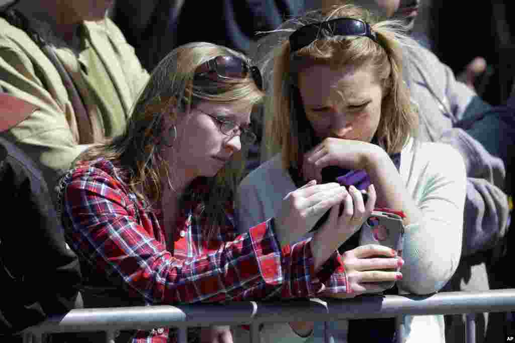 波士顿马拉松赛爆炸发生后，学护理的学生凯蒂.罗宾森，左，和梅根.比奇在奥巴马总统参加的圣十字大教堂追思会门外用电话聆听实况转播。