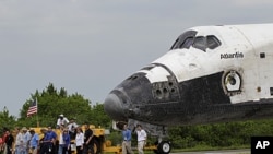 NASA workers escort space shuttle Atlantis as it is towed to the Orbiter Processing Facility for decommissioning at the Kennedy Space Center at Cape Canaveral, Florida, July 21, 2011
