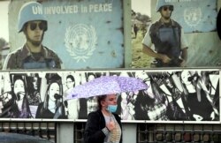 A woman wearing a face mask walks past with an umbrella during a rainy day in Sarajevo, April 21, 2020