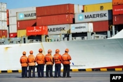 FILE - Workers stand in line next to a container ship at a port in Qingdao in China's eastern Shandong province, April 8, 2018.
