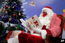 A postal worker dressed as Santa, reads letters to addressed to "Pere Noel" - Father Christmas in French - decorated with love hearts, stickers and glitter, in Libourne, southwest France, Monday, Nov. 23, 2020. (AP Photo/Francois Mori)