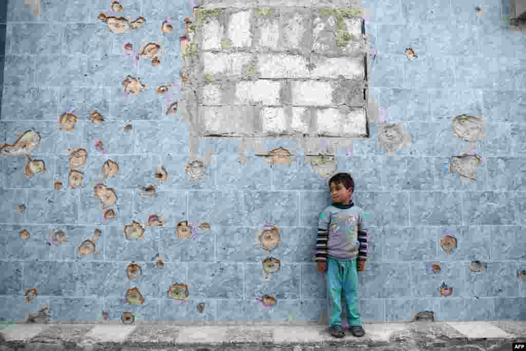 A Syrian boy stands against a wall covered in bullet holes, in the rebel-held town of Douma, on the eastern outskirts of the Syrian capital Damascus.