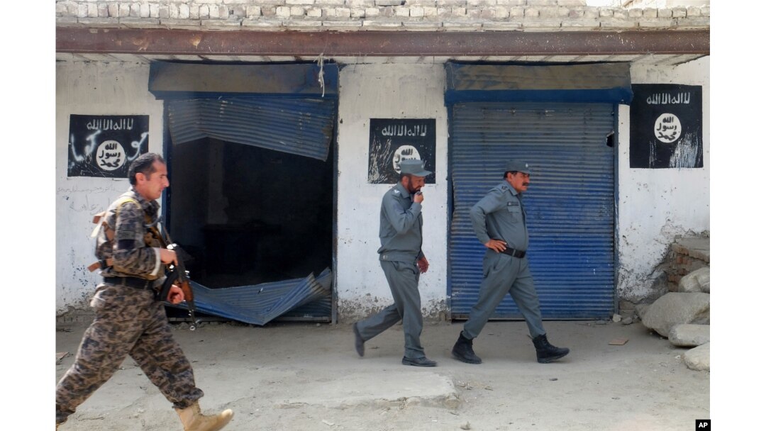 FILE - Afghan police walk past Islamic State militant flags on a wall, after an operation in the Kot district of Jalalabad province east of Kabul, Afghanistan, Aug. 1, 2016.