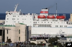 People gather holding the South Korea and U.S. national flags while North Korea's Mangyongbong-92, carrying members of North Korea's art troupe, approaches Mukho Port in Donghae, South Korea, Feb. 6, 2018.