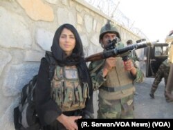 An Afghan National Army soldier and VOA reporter Ayesha Tanzeem, left, wait at a police checkpoint barrier in Achin, a district in eastern Afghanistan.