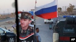 A Syrian army soldier stands at a checkpoint as a Russian military police vehicle, right, passes by near the village of Almajdiyeh, Syria, Aug. 14, 2018.