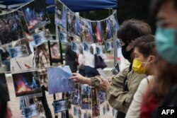 Orang-orang memeriksa gambar yang menggambarkan pengepungan kampus 2019 pada puncak protes pro-demokrasi kota di sebuah pameran di Chinese University of Hong Kong, 14 November 2020. (Foto: AFP)