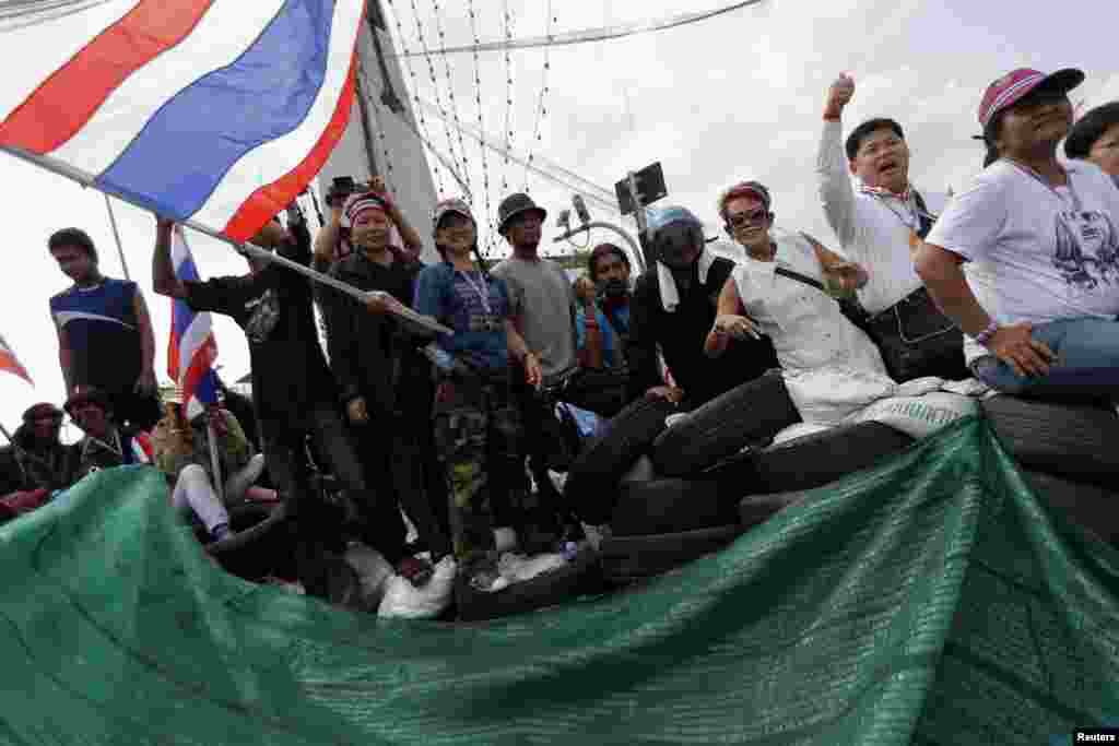 Anti-government protesters gesture from a barricade where they confront riot policemen near the Government House in central Bangkok, Feb. 14, 2014.