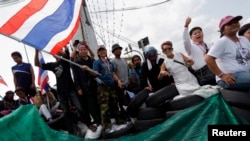 Anti-government protesters gesture from a barricade where they confront riot policemen near the Government House in central Bangkok, Feb. 14, 2014.