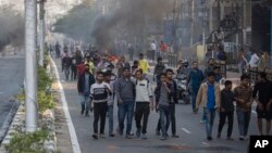 Protestors walk past burning tires defying curfew in Gauhati, India, Thursday, Dec. 12, 2019. (AP Photo/Anupam Nath)