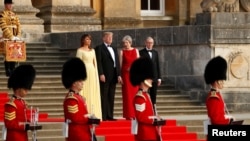 Premye Minis britanik la, Theresa May, avèk mari li, Philip (adwat), ki kanpe bò kote Pezidan Donald Trump ak Premyè Dam Lèzetazini an, Melania, nan antre Palè Blenheim nan, tou prè Inivèsite Oxford la, kote yo ta pral asiste yon dine nan konpayi kèk envite espesyal, pami yo te genyen divès òm dafè britanik. Gad britanik, an inifòm tradisyonèl, t ap asire sekirtie a. (Foto: REUTERS, 12 jiyè 2018).
