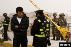 FILE - A police officer checks the identity card of a man as security forces keep watch in a street in Kashgar, Xinjiang Uighur Autonomous Region, China, March 24, 2017.