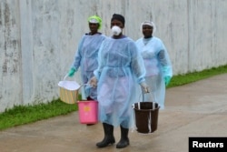 Các nhân viên y tế mang theo những chiếc xô đựng dung dịch khử trùng tại một trung tâm điều trị Ebola mới được xây dựng ở Monrovia, Liberia.