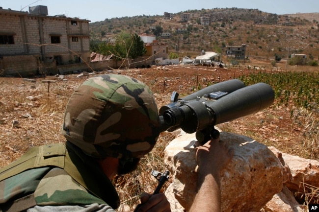 FILE - A Hezbollah fighter uses binoculars to scan for Israeli forces' positions, on the outskirts of the village of Aitaroun, near the town of Bint Jbeil, Aug. 16, 2006.