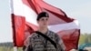 FILE - A Latvian soldier is seen holding a national flag as he waits to greet US soldiers arriving for exercises, at the airport in Riga April 24, 2014.
