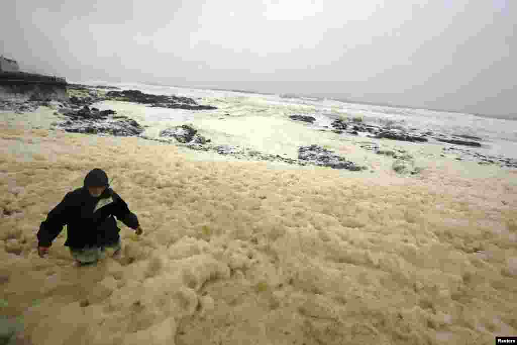 A man walks through sea foam created by storms, in the town of Portstewart on the Irish coast.