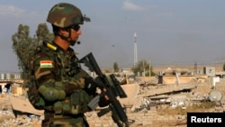 A Kurdish Peshmerga fighter walks past a house destroyed by American air strikes at Barznki village two days ago in Zummar, controlled by Islamic State (IS), near Mosul, Sept. 15, 2014. 