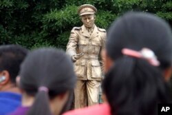 FILE - People stand in front of a statue of Gen. Aung San, late father of Myanmar National League for Democracy leader Aung San Suu Kyi, during a ceremony at a park in Yangon, Myanmar, July 19, 2015.