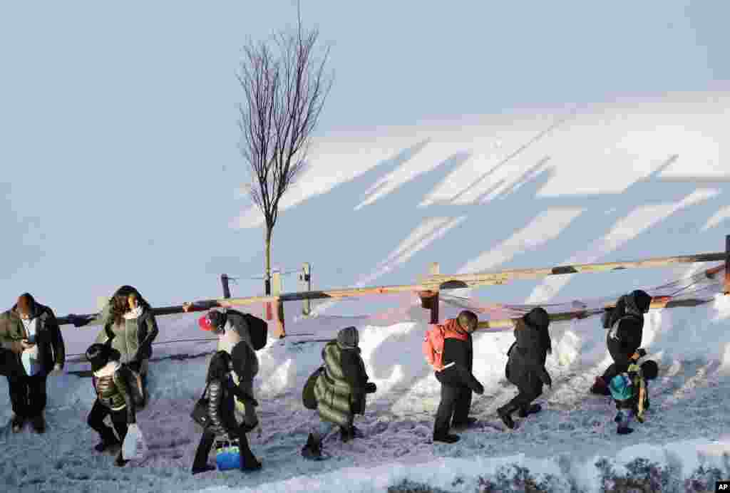 Commuters walk past piles of snow at the Broadway Junction transit hub, Monday, Jan. 25, 2016, in the Brooklyn borough of New York. (AP Photo/Mark Lennihan)