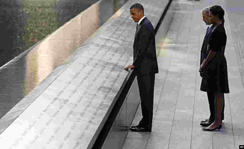 President Barack Obama touches the names of victims engraved on the side of the north pool of the World Trade Center site as former President George W. Bush, first lady Michelle Obama and former first lady Laura Bush (obscured) look on during ceremonies m